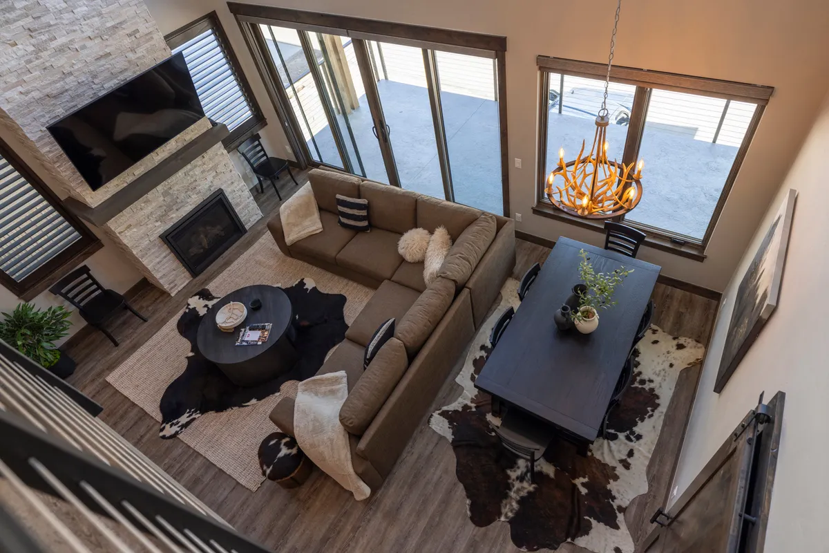 A spacious, modern living area featuring a comfortable sofa facing a stone fireplace, a stylish dining table set under a contemporary chandelier, and large windows that flood the space with natural light and showcase mountain views. The open layout invites relaxation and social gatherings, while the fireplace adds warmth and coziness for evenings after outdoor adventures.