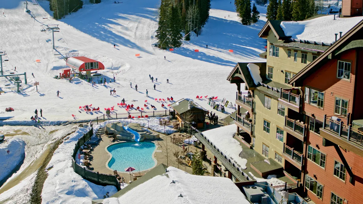 A dynamic exterior scene capturing ski slopes in the background, a swimming pool, a ski lift, and nearby lodge buildings. The vibrance of outdoor activity and direct access to resort amenities is evident, evoking the excitement of adventure just steps away.