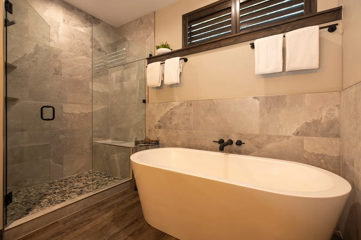 A luxuriously appointed bathroom with a freestanding soaking tub, glass shower enclosure, and textured wall tiles. The tranquil ambiance is enhanced by soft lighting, creating a spa-like setting ideal for relaxation.