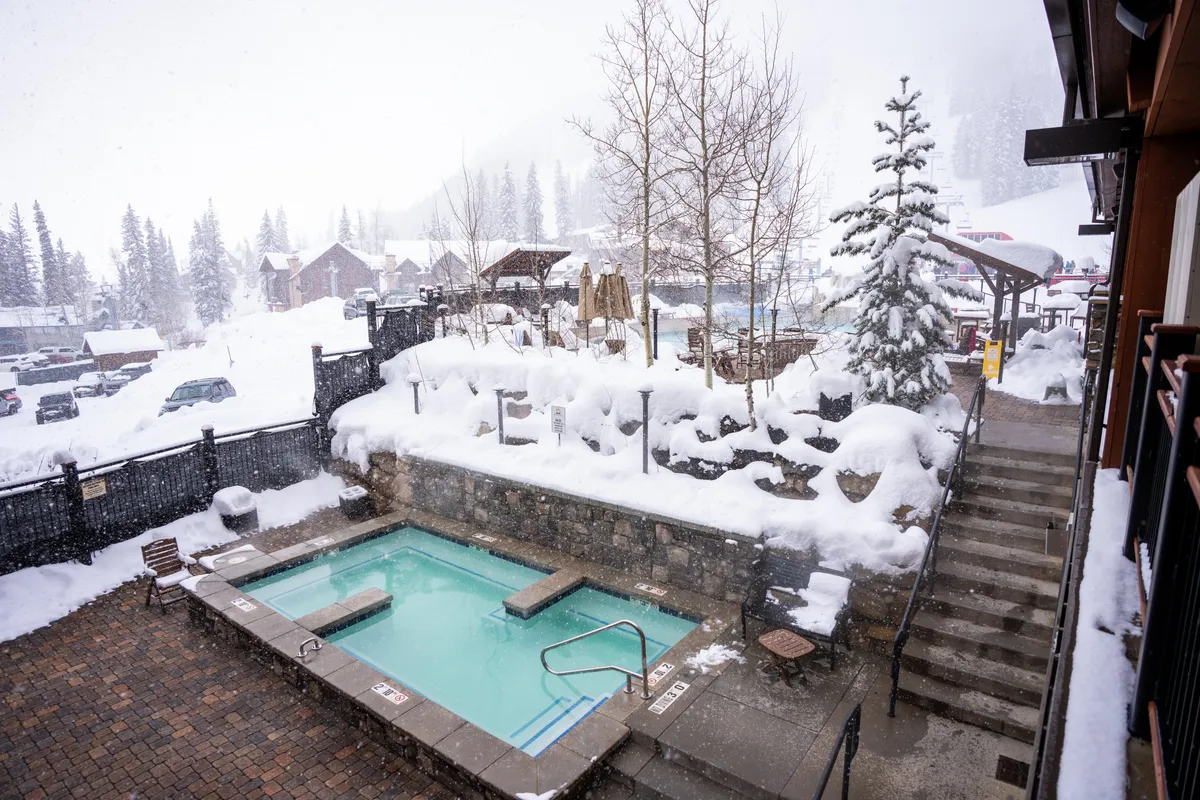 A serene winter scene of an outdoor hot tub bordered by snow-covered landscapes and trees, inviting relaxation amidst a peaceful, snowy backdrop. The setting is tranquil, suggesting memorable moments spent outdoors during colder months.
