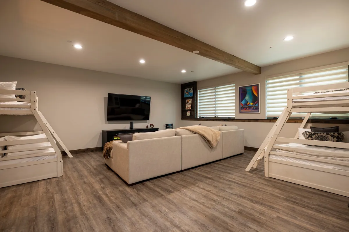 This image shows a cozy kids' room featuring bunk beds, a sofa, a television, and playful artwork on the wall. The room is arranged for both sleeping and gathering, with comfortable seating facing the TV and plenty of open floor space for games or group activities.