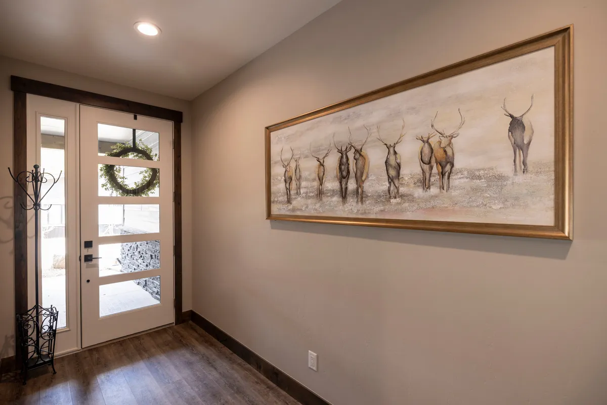 A welcoming entryway with a sturdy front door, an inviting coat rack ready for gear, and elegant artwork of an elk, setting a serene, outdoorsy tone. The space is functional for storing jackets and boots after outdoor excursions.