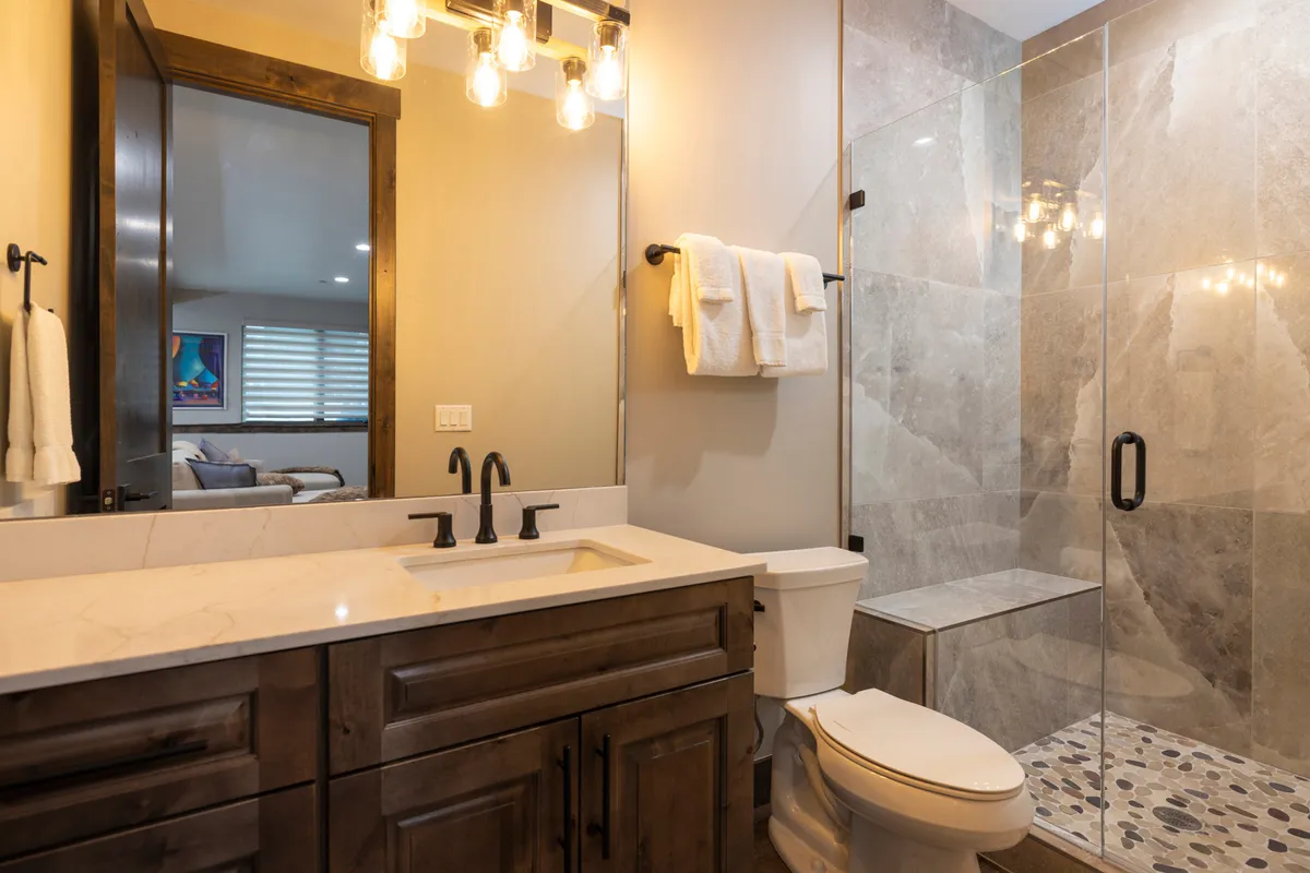 This bright, modern bathroom includes a vanity with a large sink, updated light fixtures, and a spacious shower area. The design is practical and contemporary—ideal for families and easy routines.