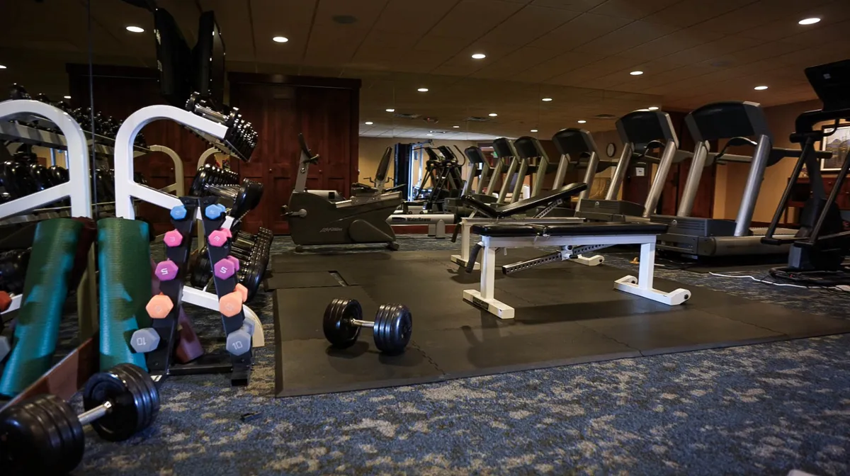 This image shows a well-equipped fitness room with dumbbells, treadmills, a weight bench, and other exercise machines. The space is bright and motivational, inviting guests to stay active indoors regardless of the season.