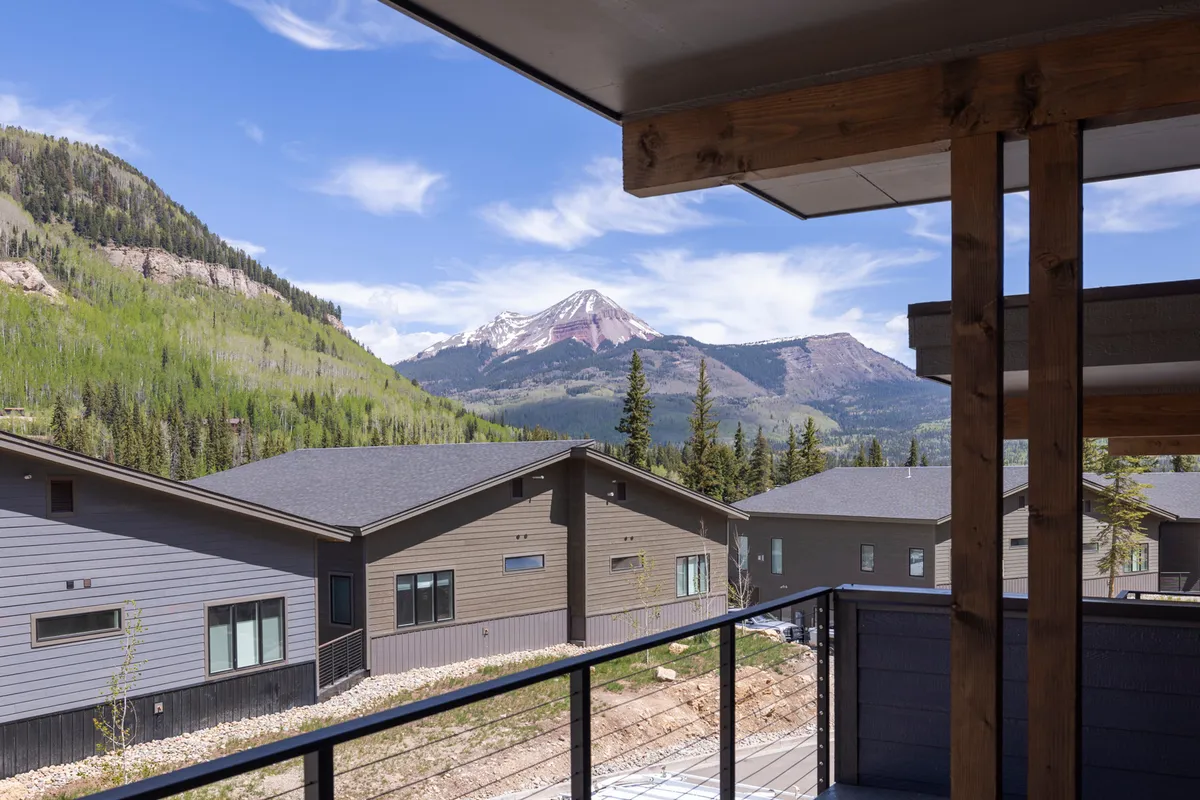 A tranquil exterior view featuring a majestic mountain in the background, modern houses nearby, and lush green landscape. The image highlights direct access to natural surroundings and hints at the proximity to hiking and outdoor activities.