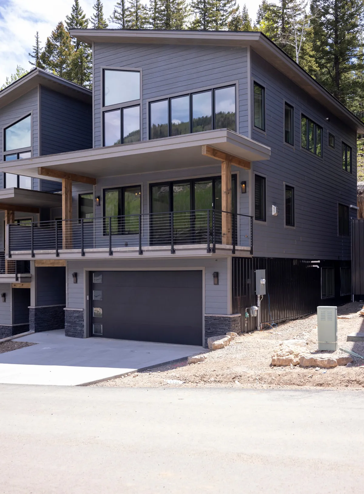 An exterior view of the home showcasing large windows, wooden accents, and a balcony with a railing. The balcony is set up for gatherings, with scenic vistas perfect for sunset watching or grilling. The overall effect is modern yet welcoming, hinting at the mountain environment and inviting outdoor living.