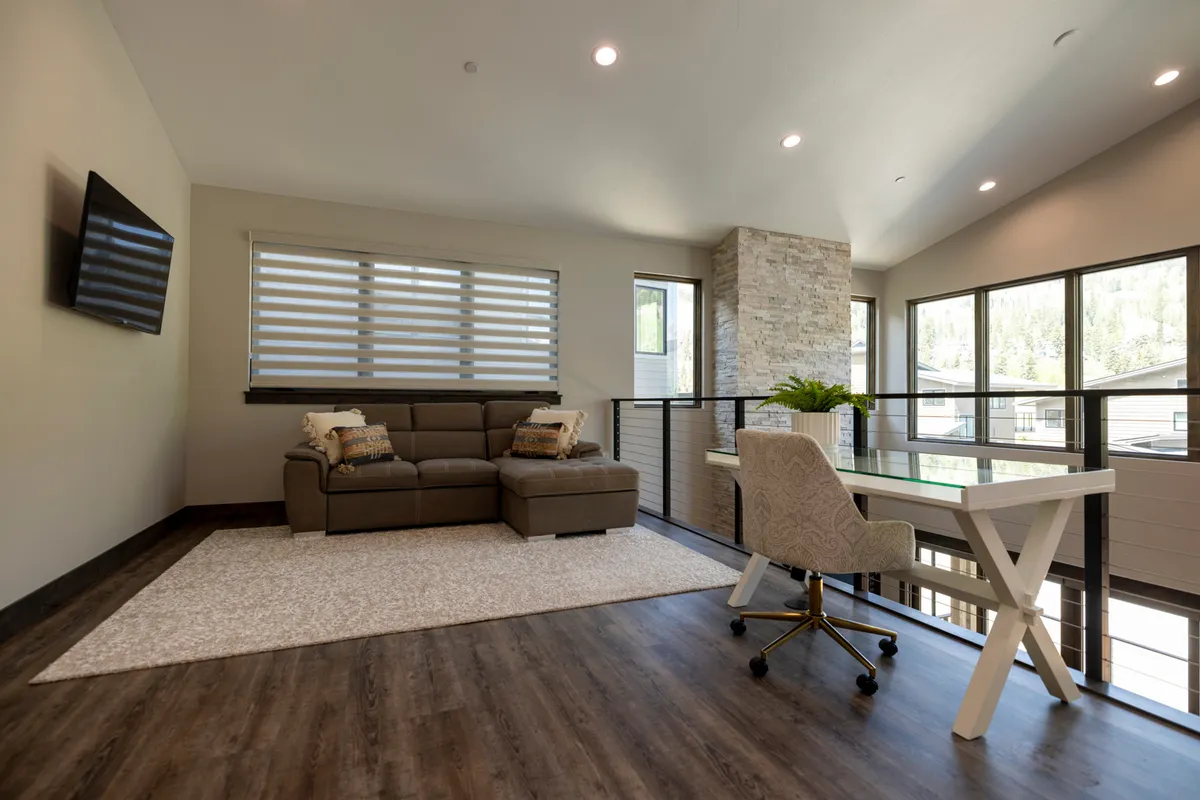A bright, modern living space with a large sectional sofa, a writing desk for catching up on work or journaling, a striking stone feature wall, and expansive windows offering beautiful natural light and glimpses of the outdoors. The atmosphere combines comfort for relaxation with functional spaces for planning the next day's activities.