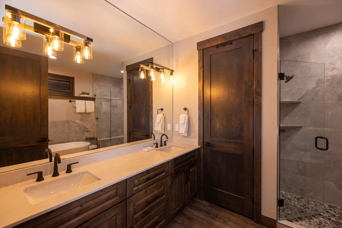 A modern bathroom with a spacious double-sink vanity, large framed mirror, shower area, and stylish wooden cabinetry. The calm, rejuvenating mood evokes a spa-like experience ideal for shared use.